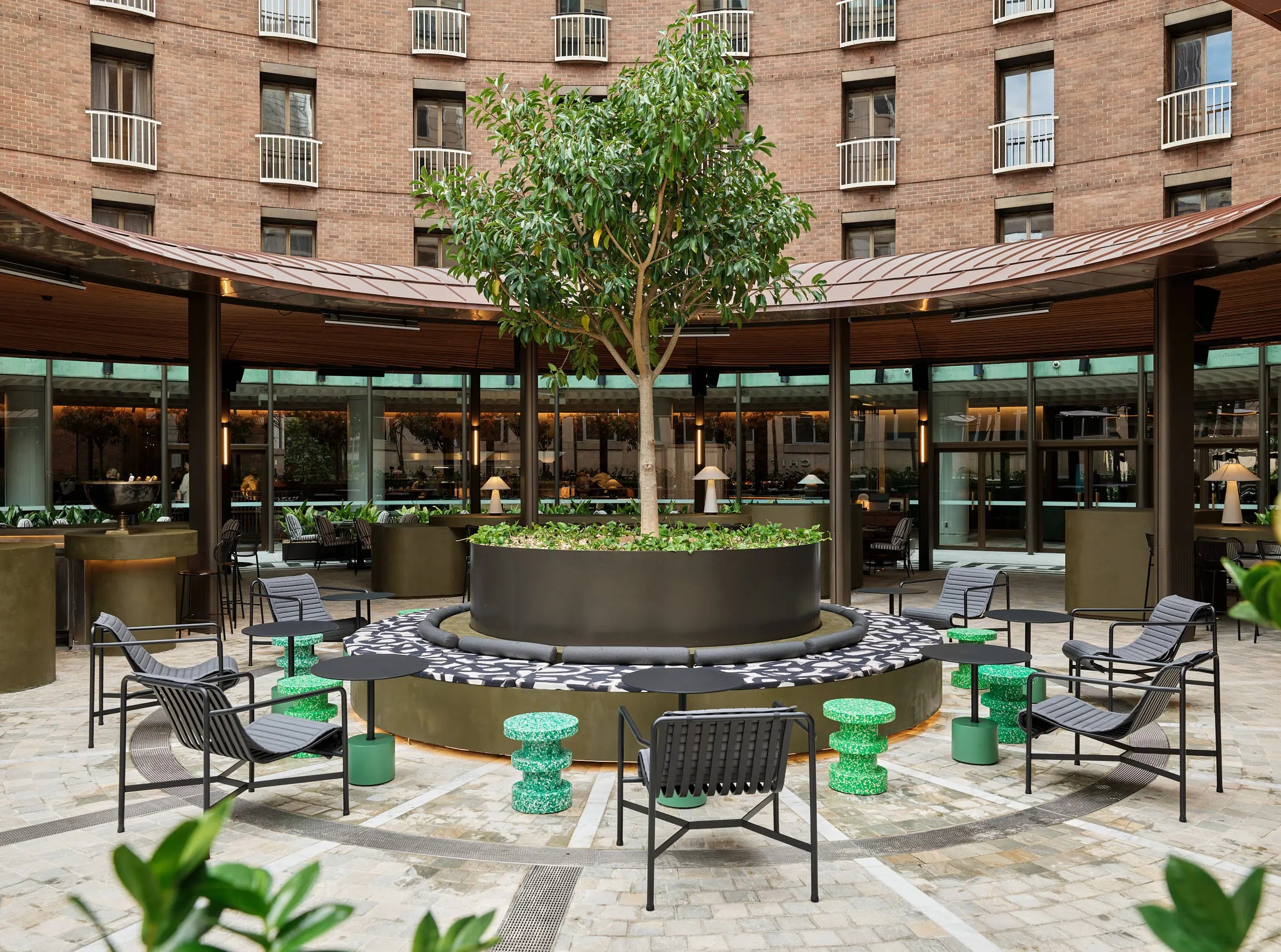 Outdoor courtyard with chairs, tables, and a tree in front of a building.