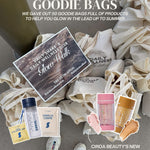 Goodie bags with Daily Wellness Club products and Ciroa Beauty shimmer sticks on a gray surface.